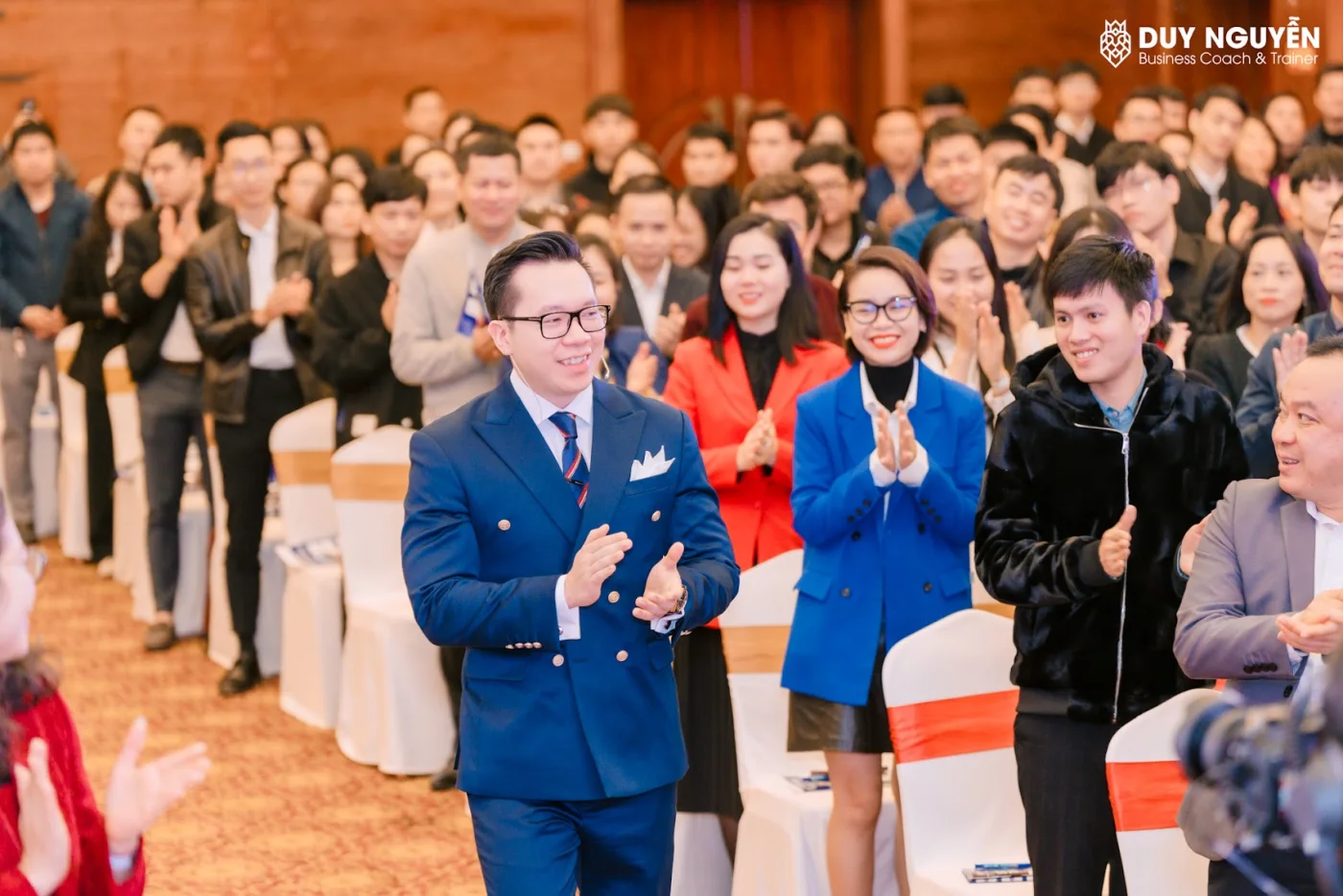 Coach Duy Nguyễn đi giữa hàng ghế trong một hội trường đông người